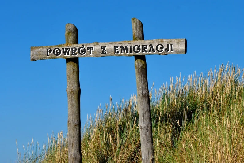Drewniany drogowskaz z napisem „Powrót z emigracji”, symbolizujący decyzję o powrocie do Polski po latach za granicą